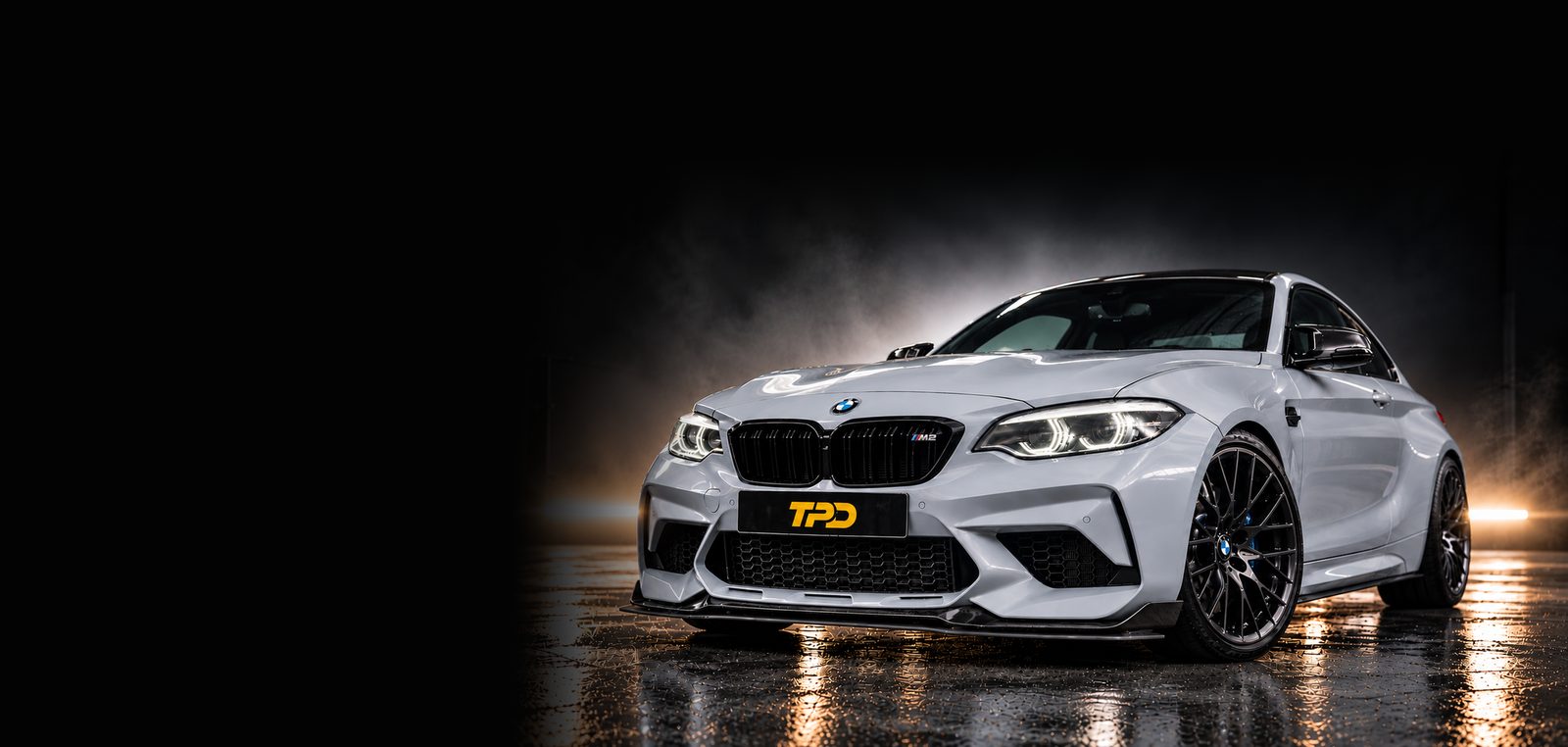 White BMW M2 on a wet floor under amber lights